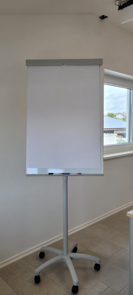 Flipchart Ein leerer Flipchart-Ständer mit Rollen in einem hellen Raum.