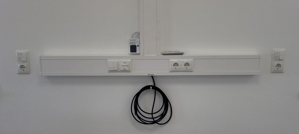 Technik Weißes Wandpaneel mit Steckdosen und einem Kabel, das herunterhängt.