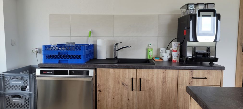 Küche Küchenzeile mit Geschirrspüler, Kaffeemaschine und Spüle, blaue Kiste an der Wand.