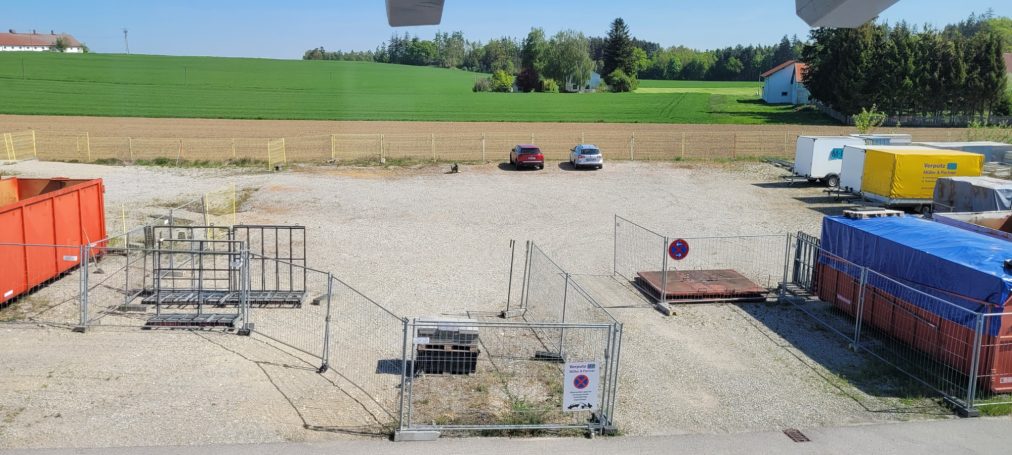 Großer Parkplatz Blick auf einen unbefestigten Platz mit Containern und parkenden Fahrzeugen.