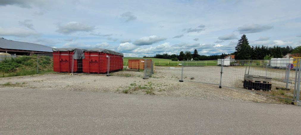 kleiner Parkplatz Blick auf einen Lagerplatz mit mehreren Containern und leerem Grundstück.